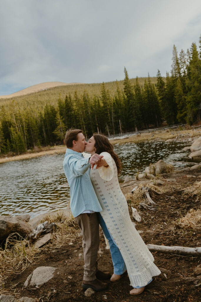 man and woman kissing in front of lake engagement session